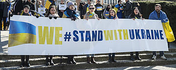 Demonstranten halten ein Banner mit der Aufschrift "We stand with Ukraine"