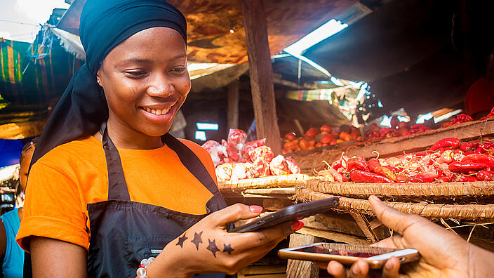 young african woman selling tomatoes in a local african market receiving payment via mobile phone transfer